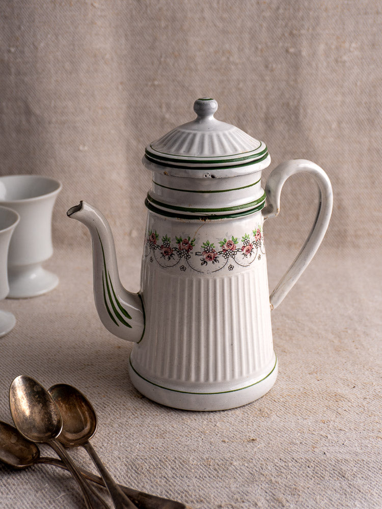 Vintage white ceramic teapot with green floral detail and antique B.B. Frères enamel French coffee pot, teaspoons, and cups behind.