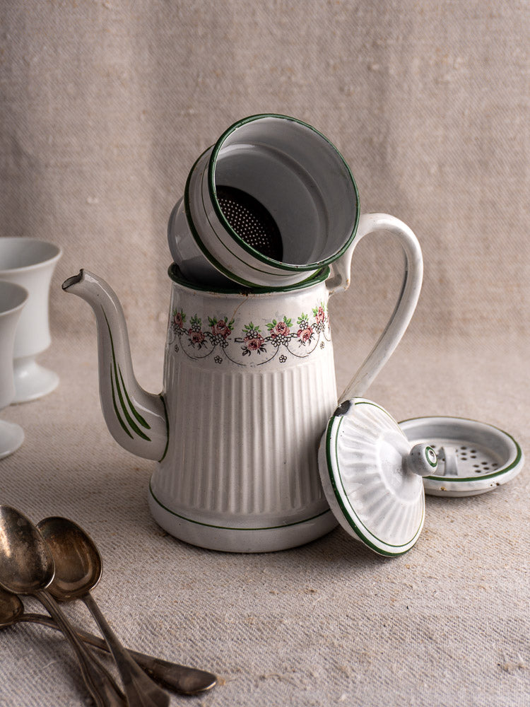 Antique French enamel coffee pot by B.B. Frères, vintage white with floral accents, lid off, on beige surface with spoons and cups.