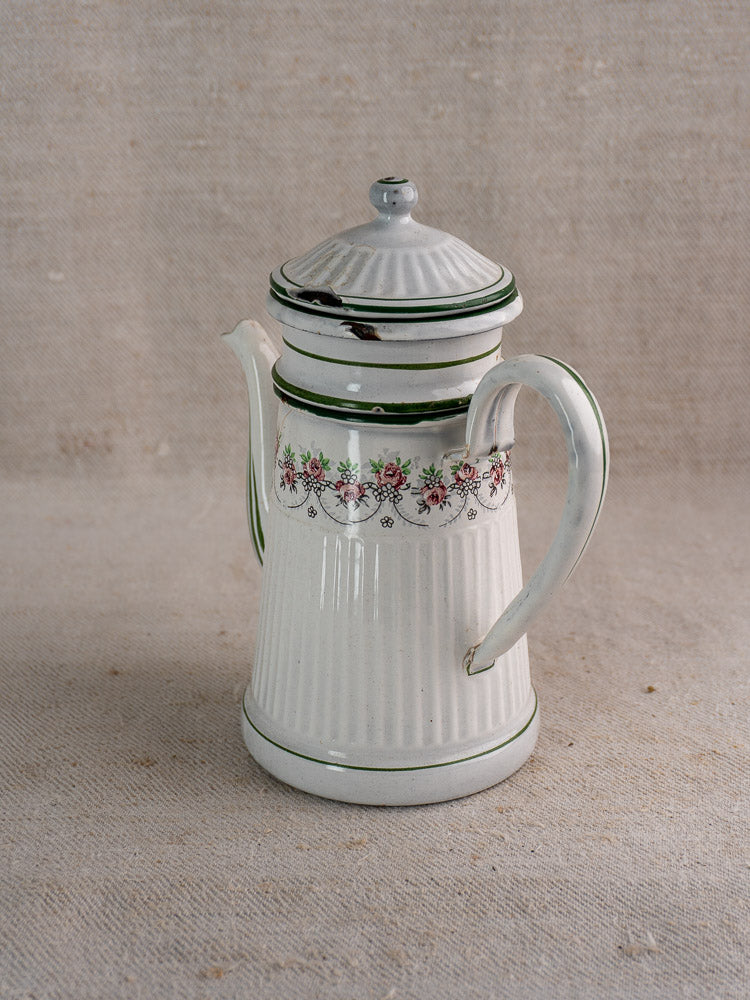 Antique French enamel coffee pot by B.B. Frères with green trim and floral design on neutral fabric background.