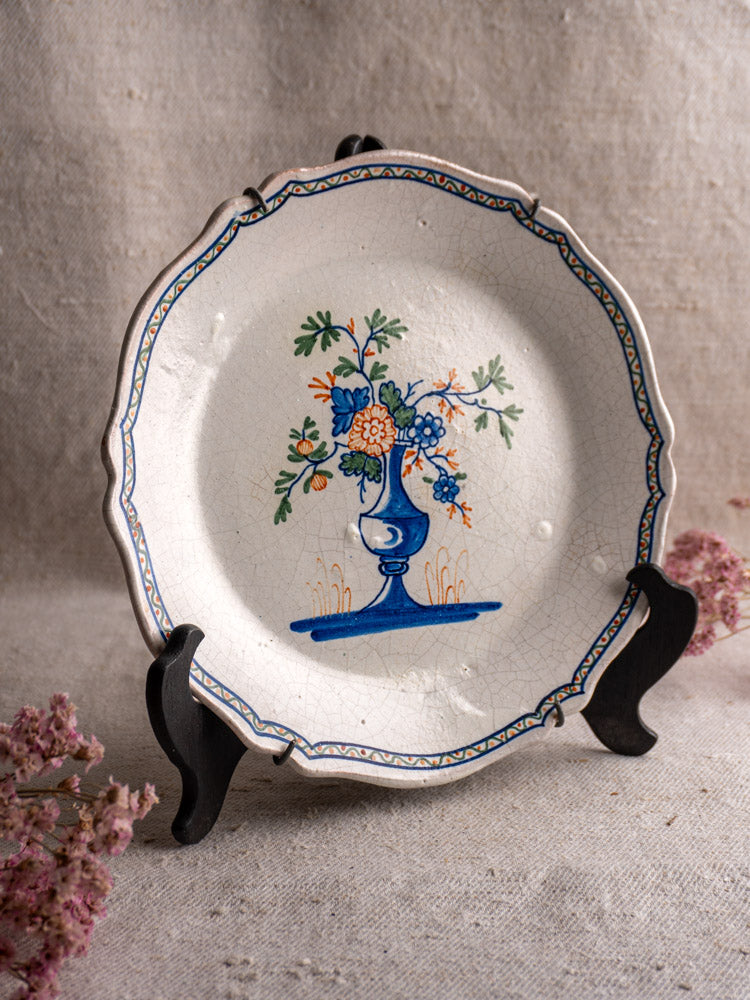 Antique French faience plate with scalloped edge, hand painted polychrome floral bouquet, on black stand.