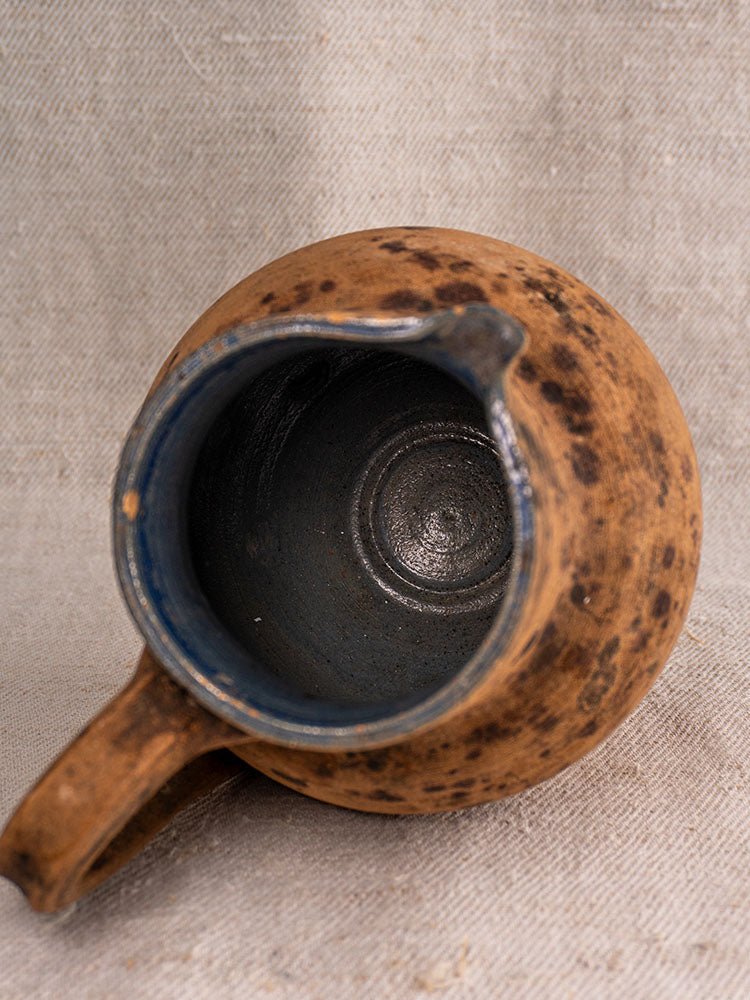 Top view of a mid-19th century French terracotta pitcher with handle, spout, and cobalt blue glazed interior on light fabric.