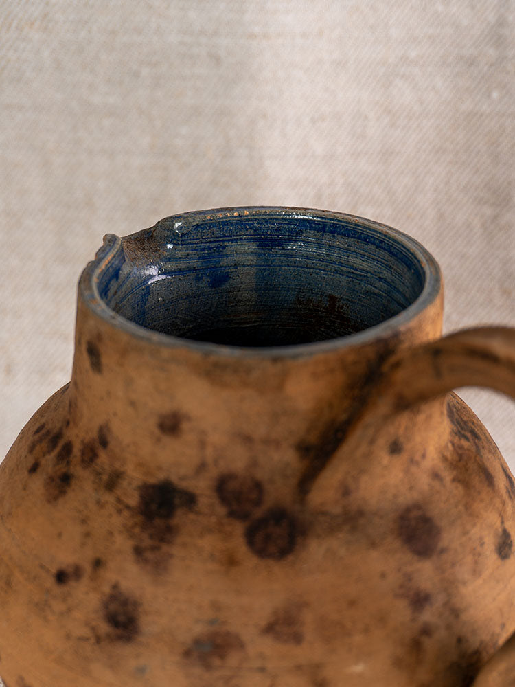 Antique French terracotta pitcher, mid-19th century, dark spots, cobalt blue glazed interior, small spout on light textured fabric.