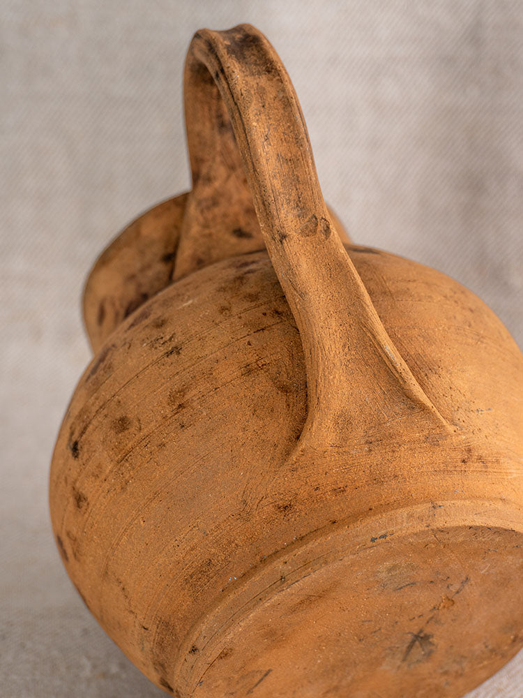 Antique French terracotta pitcher with natural imperfections and cobalt blue glazed interior on woven fabric background.
