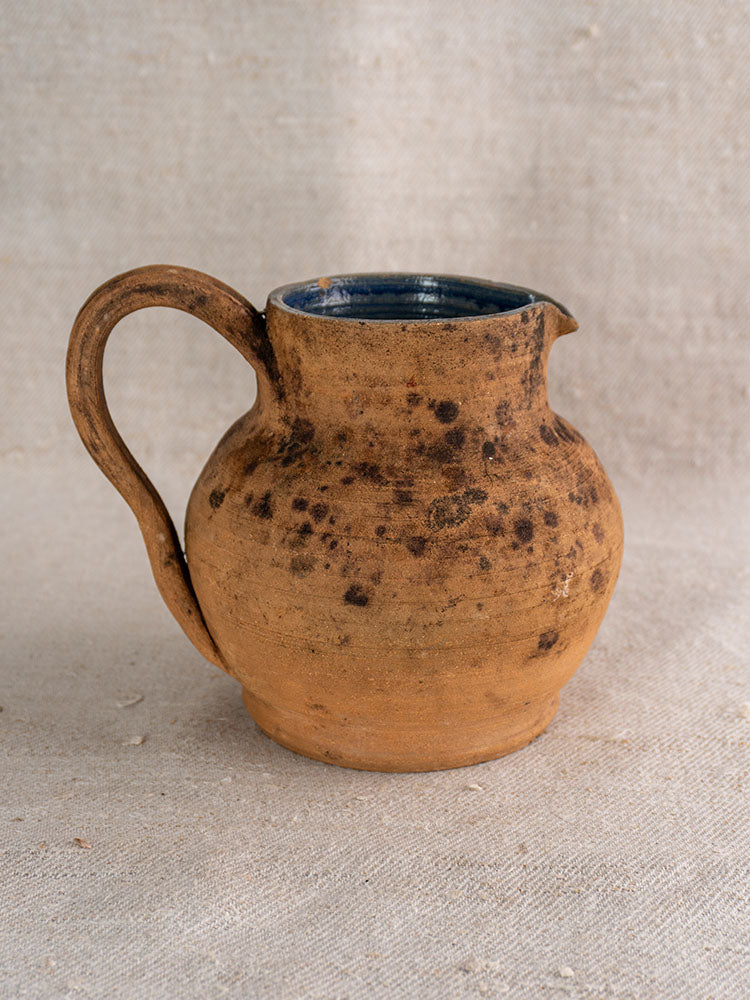 Mid-19th century French terracotta pitcher with cobalt blue glazed interior on beige textured fabric.