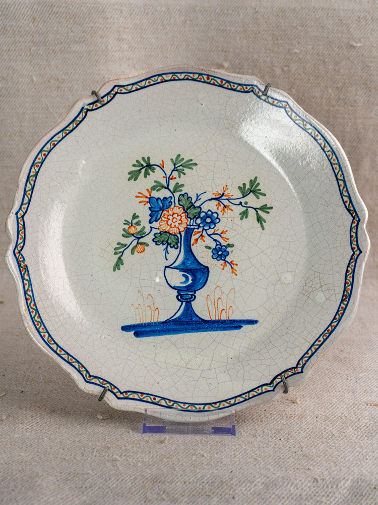 Antique French faience plate, c. 1850, scalloped edge, polychrome floral vase center, blue-orange border detailing.