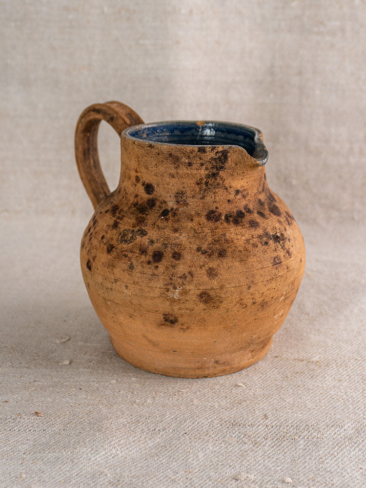 Antique French terracotta pitcher with wide body, sturdy handle, weathered surface, and cobalt blue glazed interior.