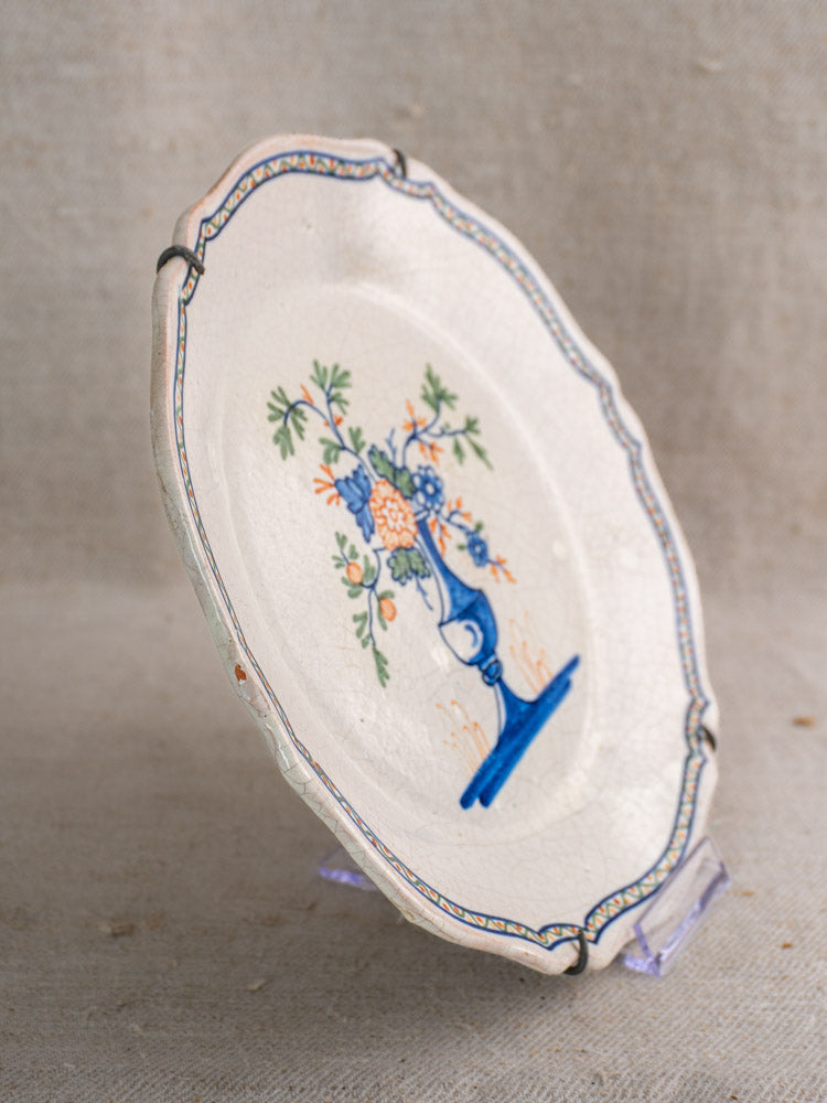 Antique French faience plate, c. 1850, hand-painted florals, scalloped edge, crackled glaze on clear stand against neutral backdrop.