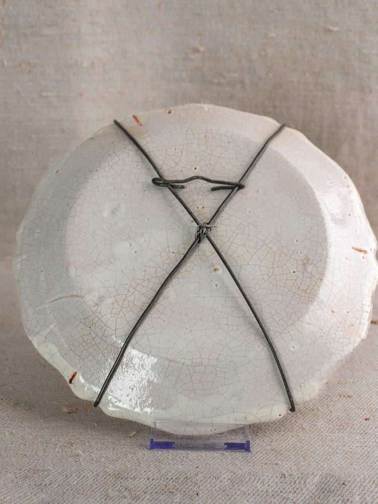 Antique French faience plate, hand painted vase bouquet, visible crazing and wire repairs, on beige fabric background.