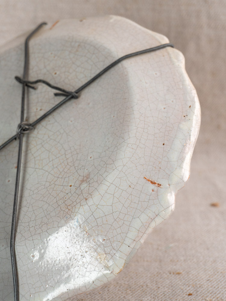 Antique French faience plate with cracked white glaze, hand painted bouquet, wire repairs, and brown patina on beige fabric.