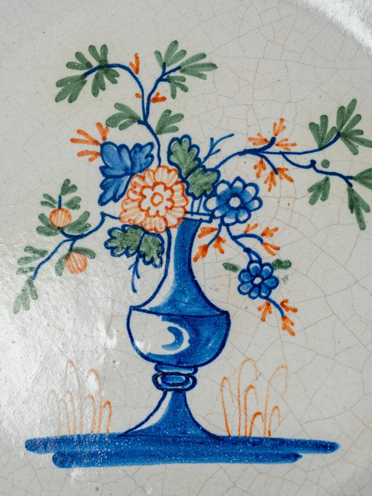 Antique French faience plate, hand-painted with a blue vase of orange and blue flowers on crackled white ceramic.