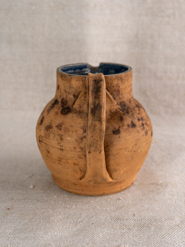 Antique French terracotta pitcher, mid-19th century, cobalt blue interior, weathered brown exterior on beige fabric.
