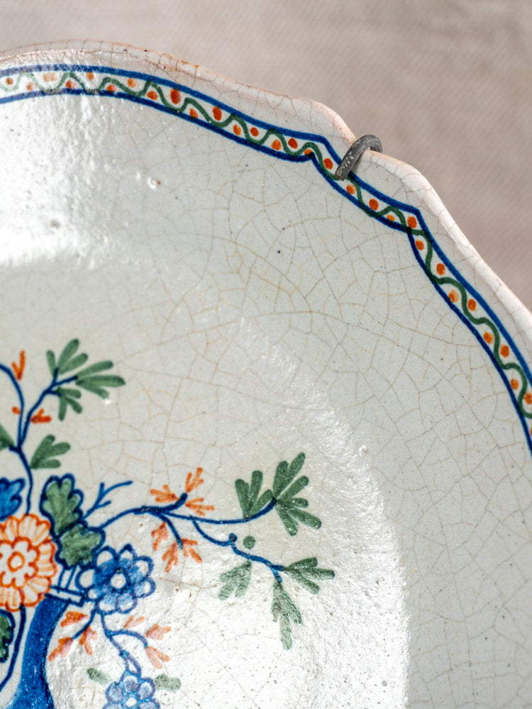 Antique French faience plate with polychrome floral design, scalloped chipped edge, crackle glaze, and rim metal hanger.