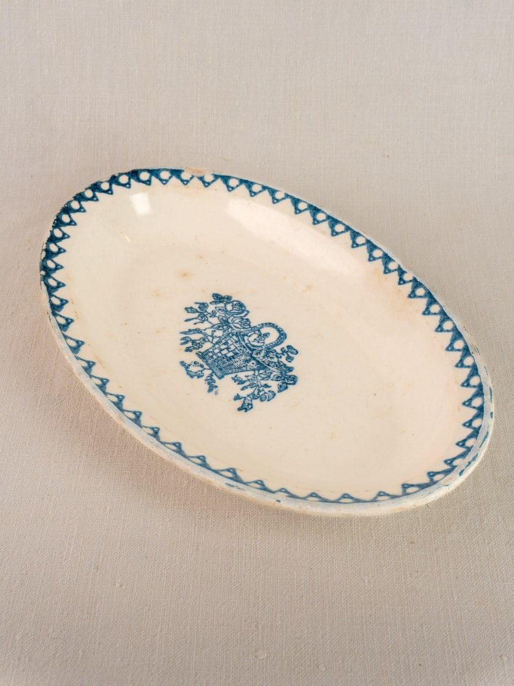 Antique French faience oval plate by Bertrand Opaque Surfine with blue flower basket on neutral fabric background.