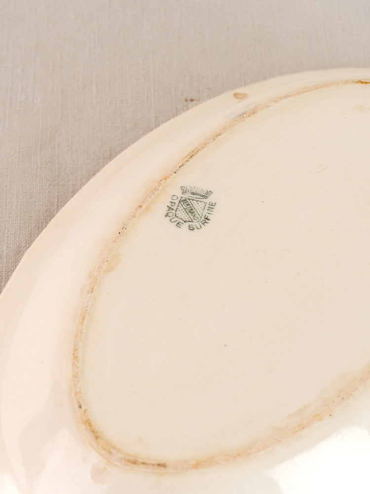 Underside of antique French faience oval plate, Bertrand Opaque Surfine, blue flower basket motif on gray fabric surface.