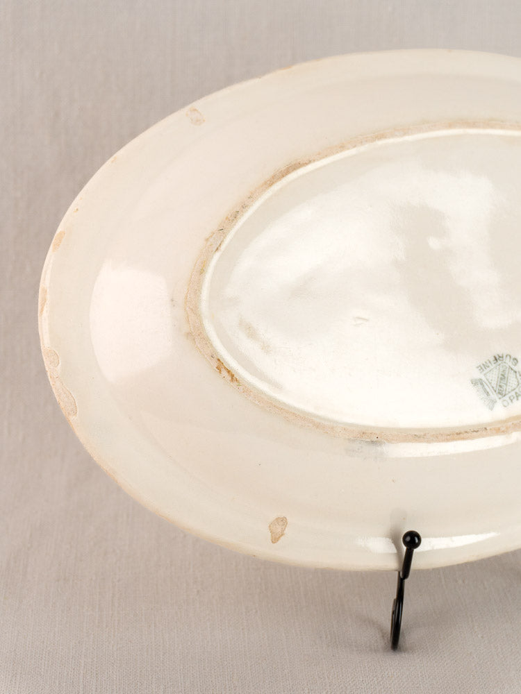 Antique French faience oval plate, Bertrand Opaque Surfine, shown underside with edge wear and faint green mark on gray fabric.