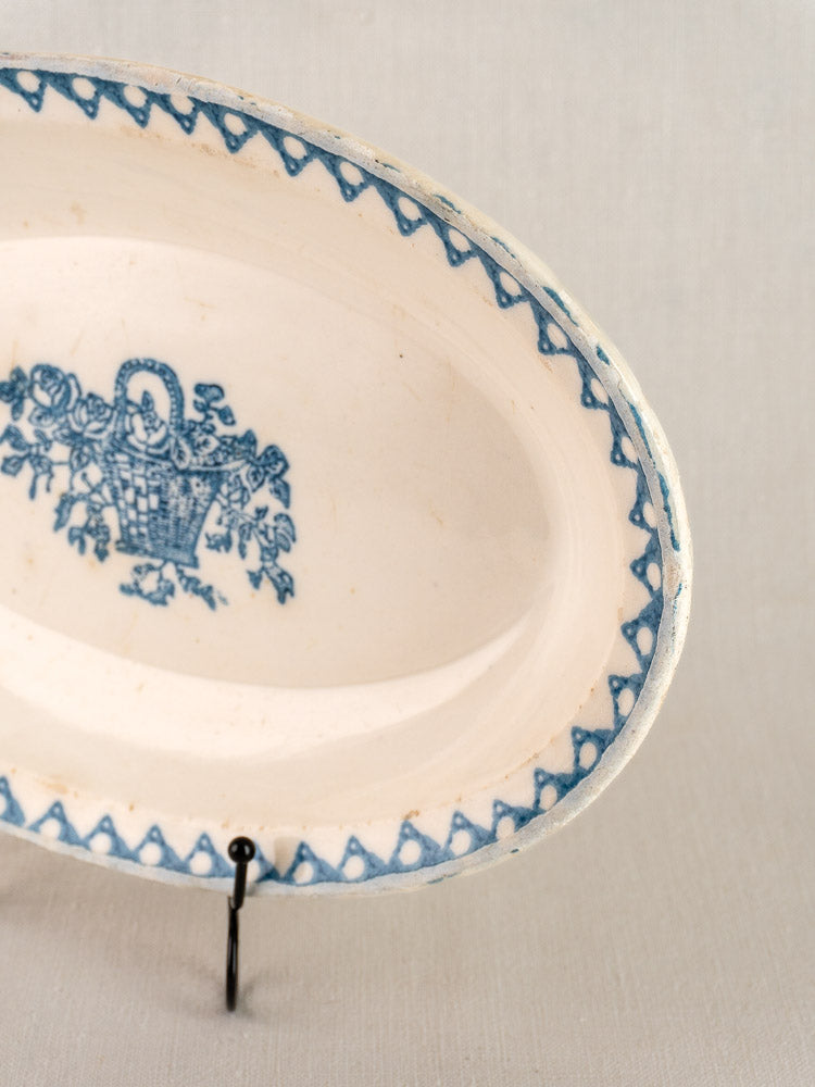 Antique French faience oval plate, Bertrand Opaque Surfine, blue floral basket motif, on stand with neutral background.