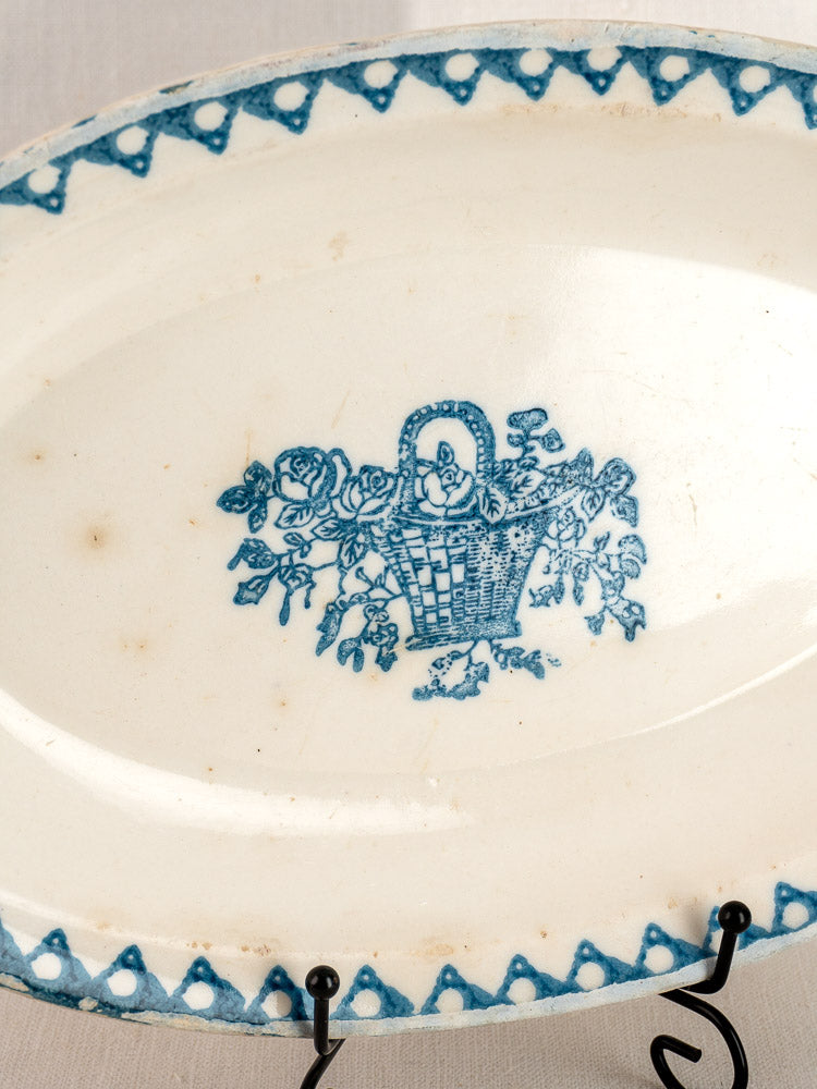 Antique French faience oval plate by Bertrand Opaque Surfine with blue floral basket motif and border on black metal stand.