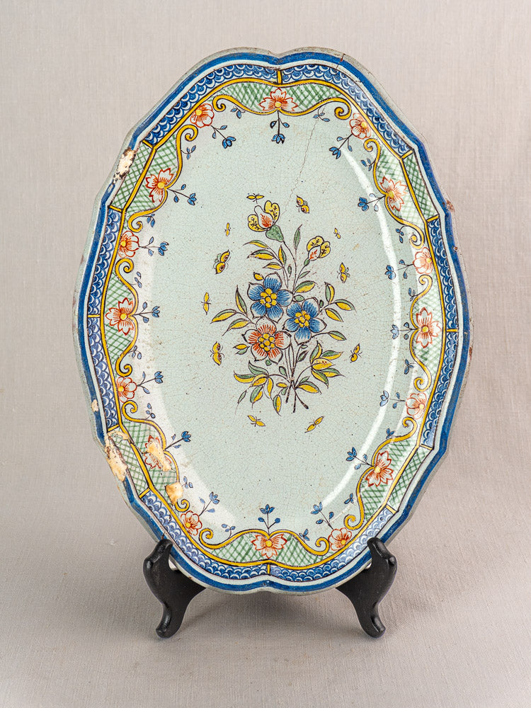 18th-century French Orléans Faience platter with scalloped edges and floral motif on black stand against neutral backdrop.