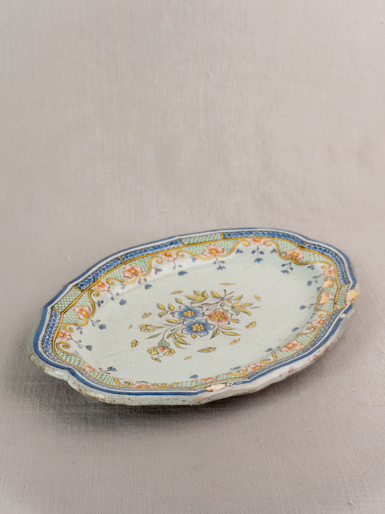 18th-century French Orléans faience platter with scalloped edges and floral motifs on a neutral fabric background.