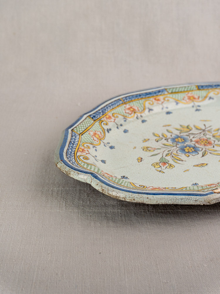 Antique French Orléans faience platter with polychrome floral design and ornate border, partial view on neutral fabric background.