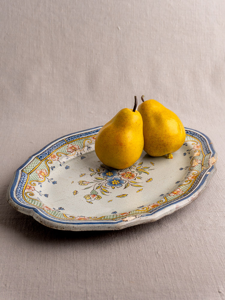Antique French Orléans faience platter, 18th-century polychrome cul noir, floral motif, blue border; two yellow pears on gray fabric.