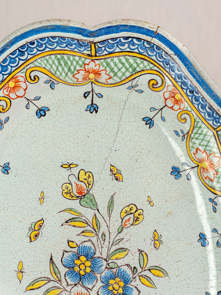 Antique French Orléans faience platter with blue, yellow, and red florals, green accents, blue scalloped edge, fine glaze cracking.
