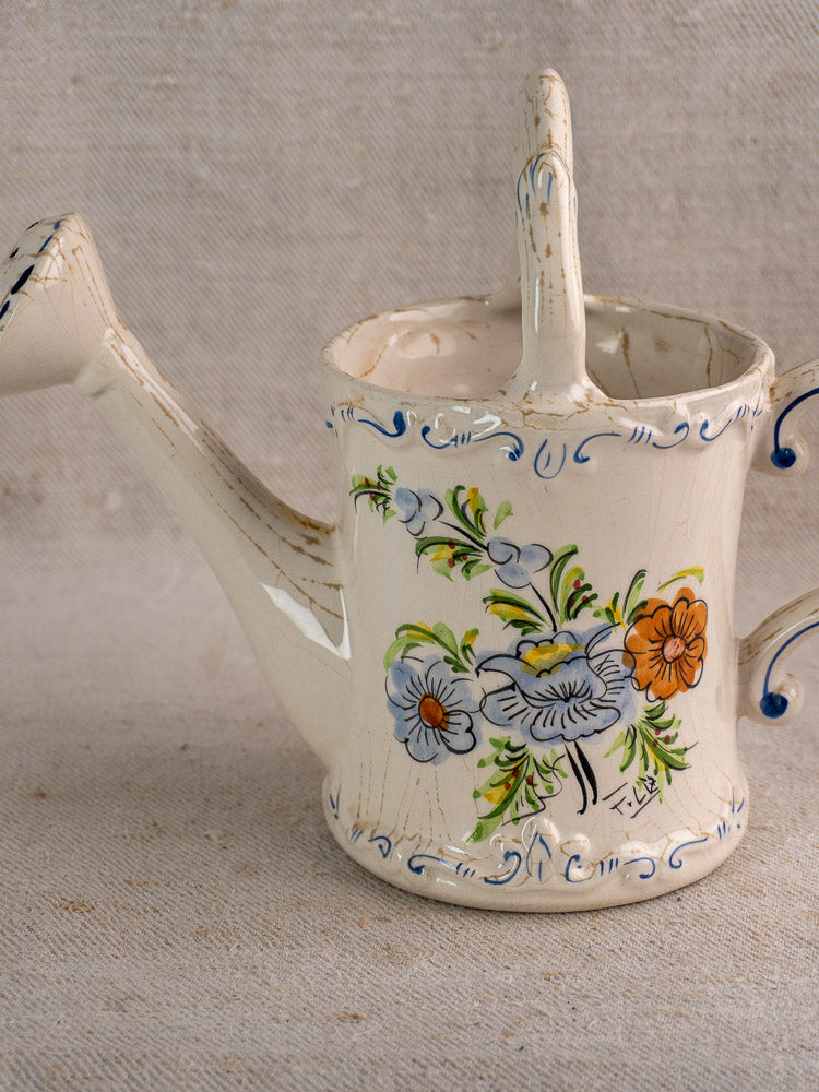 Cream-colored French faience watering can with ornate handle, hand-painted floral motifs, textured finish.