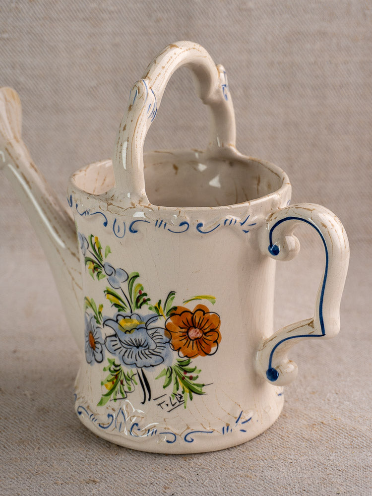 Vintage French faience watering can with blue, orange, and green floral motifs on cream ceramic.