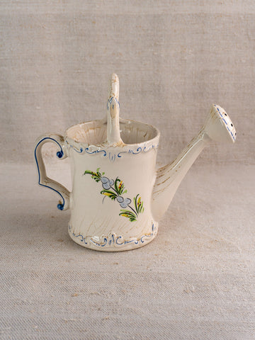 Vintage French faience watering can, cream with blue and green hand-painted florals, on beige textured surface.
