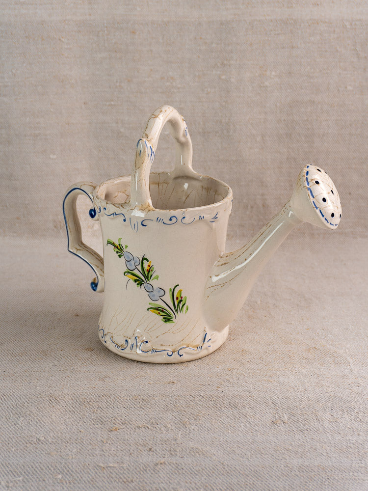 Vintage French faience watering can with hand-painted blue and green floral motifs on beige textured surface.