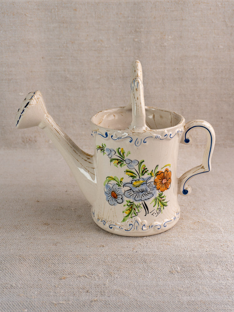 Cream ceramic French faience watering can with hand-painted blue, orange, and green floral motifs.