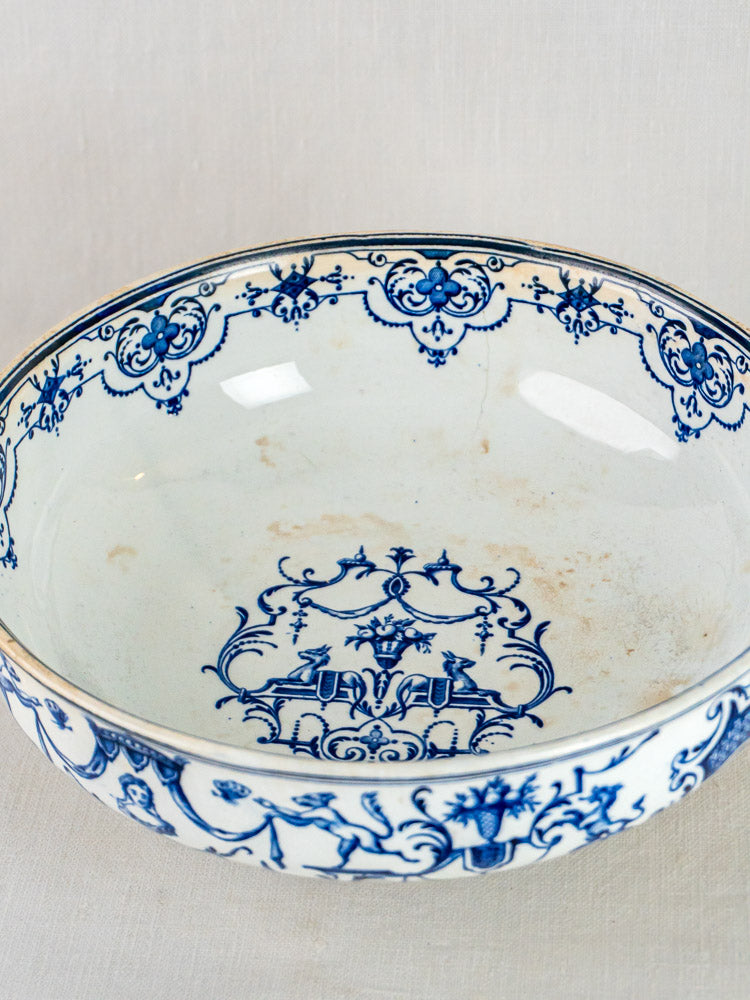Antique French blue faience bowl with intricate floral and scroll motifs on white, on neutral surface.