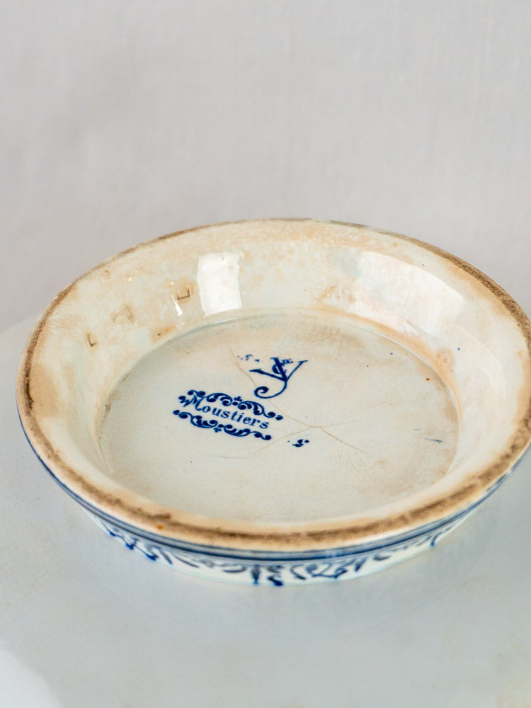 Shallow round ceramic dish with worn beige rim and blue “Moustiers” decoration, antique French faience.