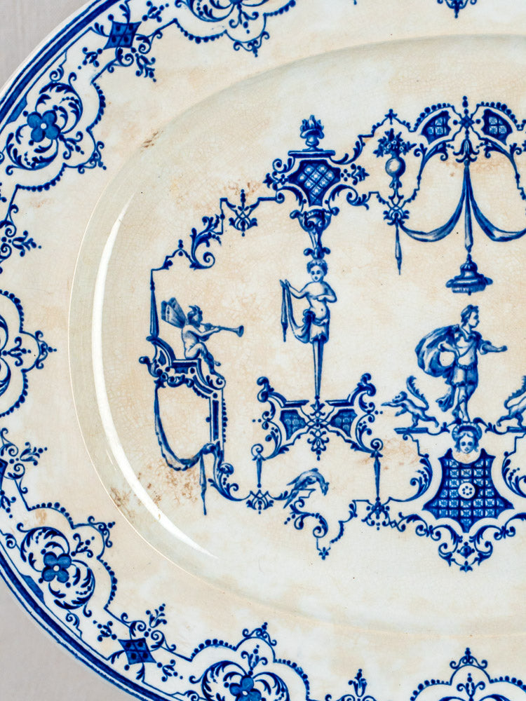 Decorative ceramic plate from Jules Vieillard Bordeaux Moustiers, intricate blue patterns and whimsical figures on cream background.