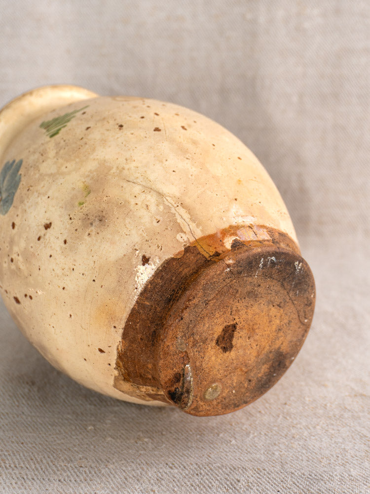 Base of mid-19th century French faience pitcher, hand-painted florals, beige finish, rustic brown bottom; shown on neutral fabric.