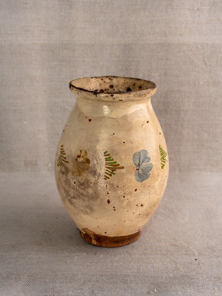 Antique French faience pitcher with polychrome floral motifs and cream glaze, displayed on neutral fabric.