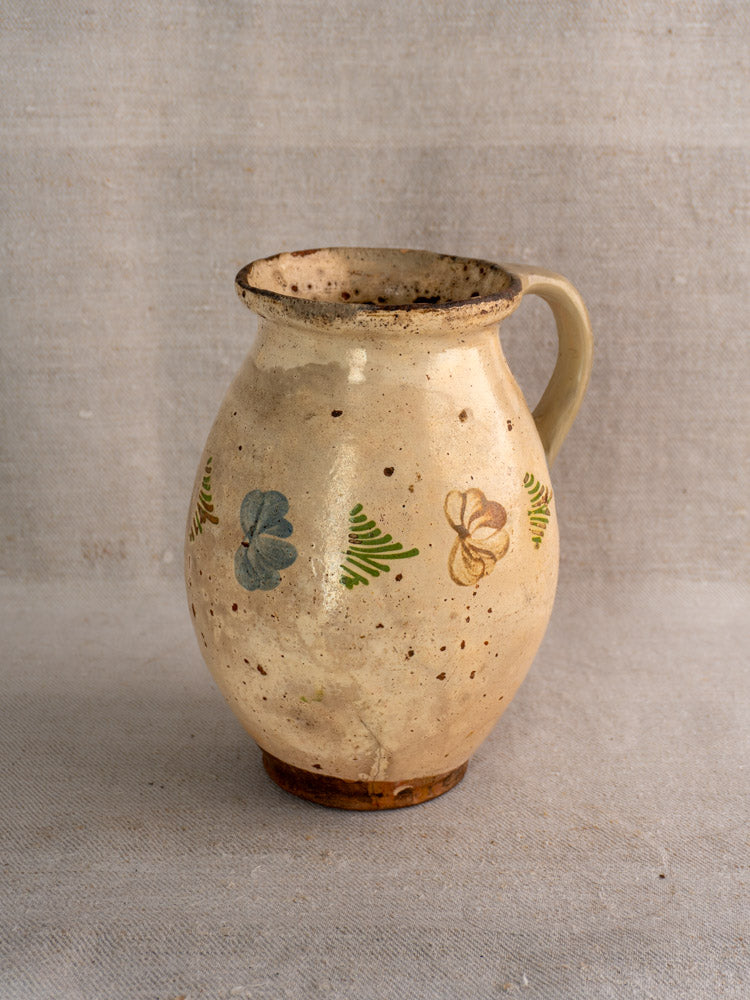 Antique French faience pitcher, mid-19th century, cream with brown speckles and polychrome floral designs on fabric background.