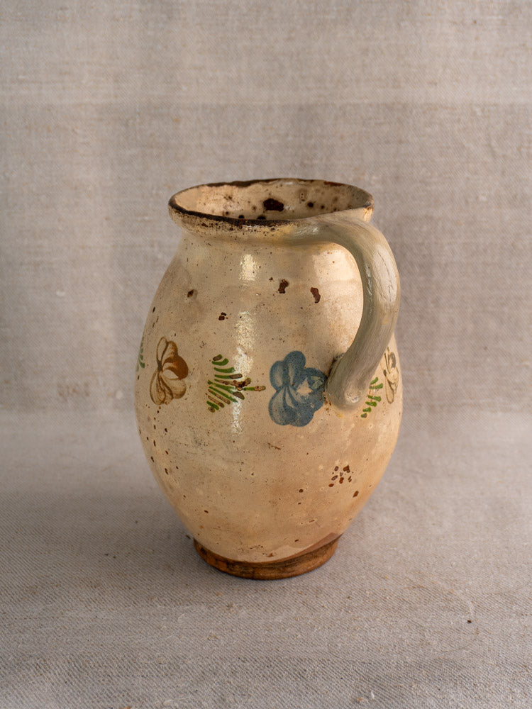 Mid-19th century French faience pitcher with hand-painted floral motifs and single handle on neutral fabric background.