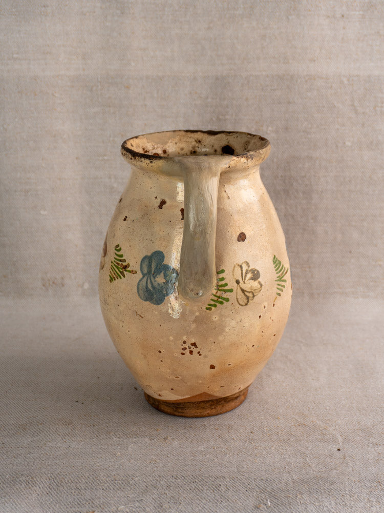 Antique French faience pitcher with hand-painted blue and brown florals, green leaves, handle, rustic cream finish. Mid-19th century.