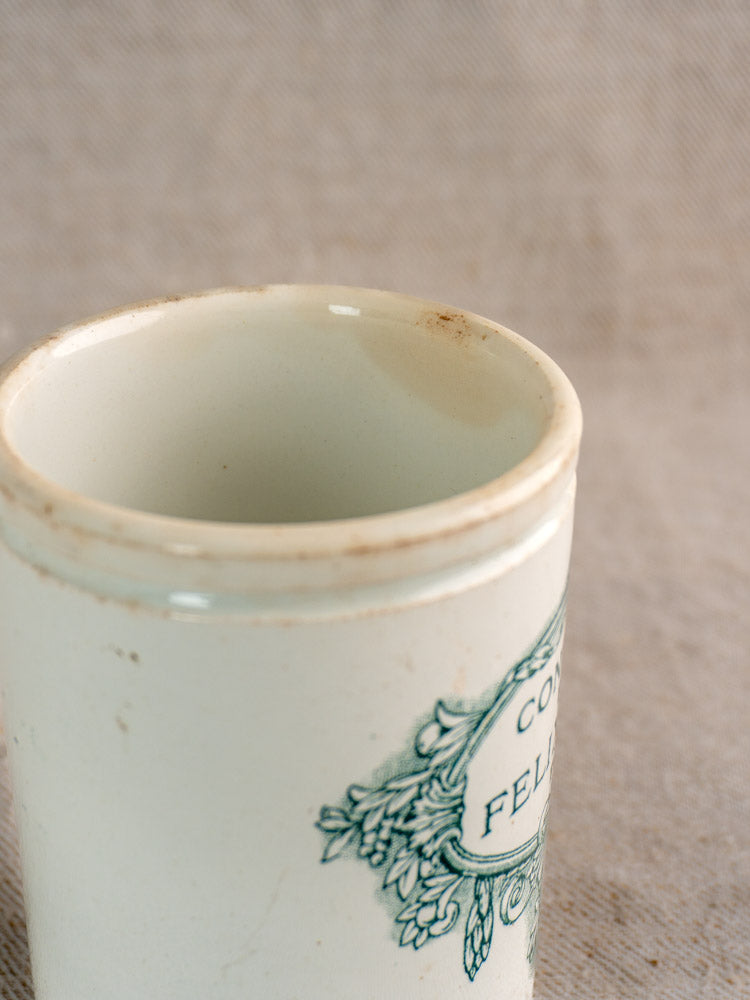 Antique French Felix Potin jam pot with green accents and rim stains, on a textured beige background.