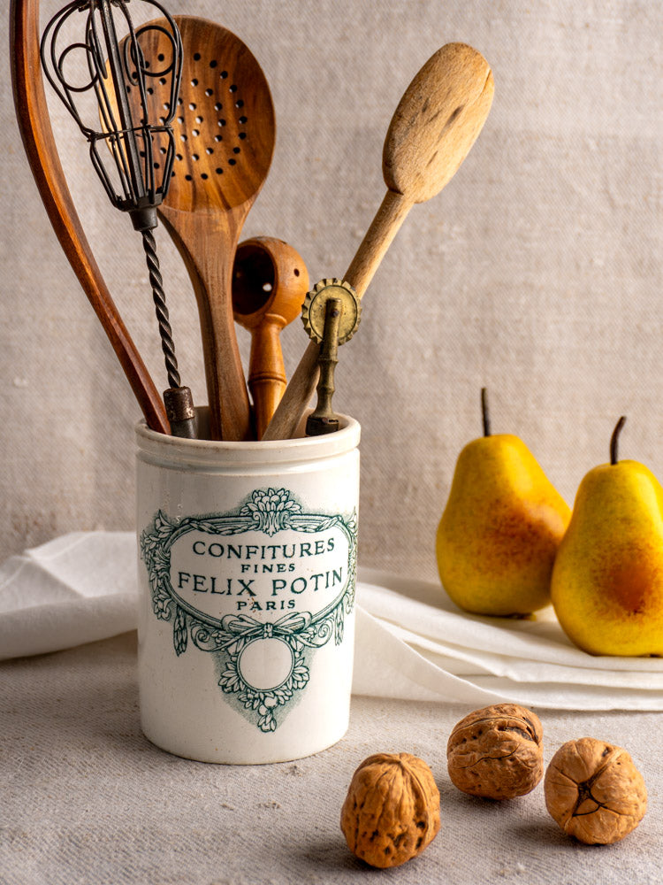 Antique French Felix Potin jam pot holding utensils, styled with yellow pears, walnuts, and soft fabric backdrop.