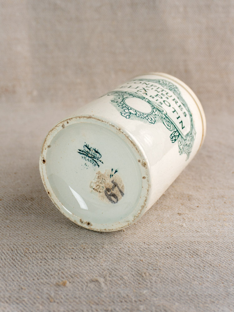 Antique French Felix Potin jam pot labeled "Confitures Fines Paris" with green decorative lettering, on beige textured fabric.