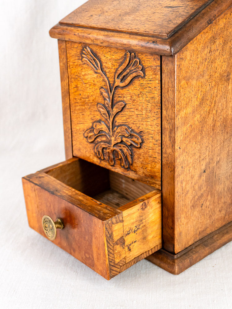 Antique French carved walnut flour and salt box with leaf motif, brass handle, on light fabric.