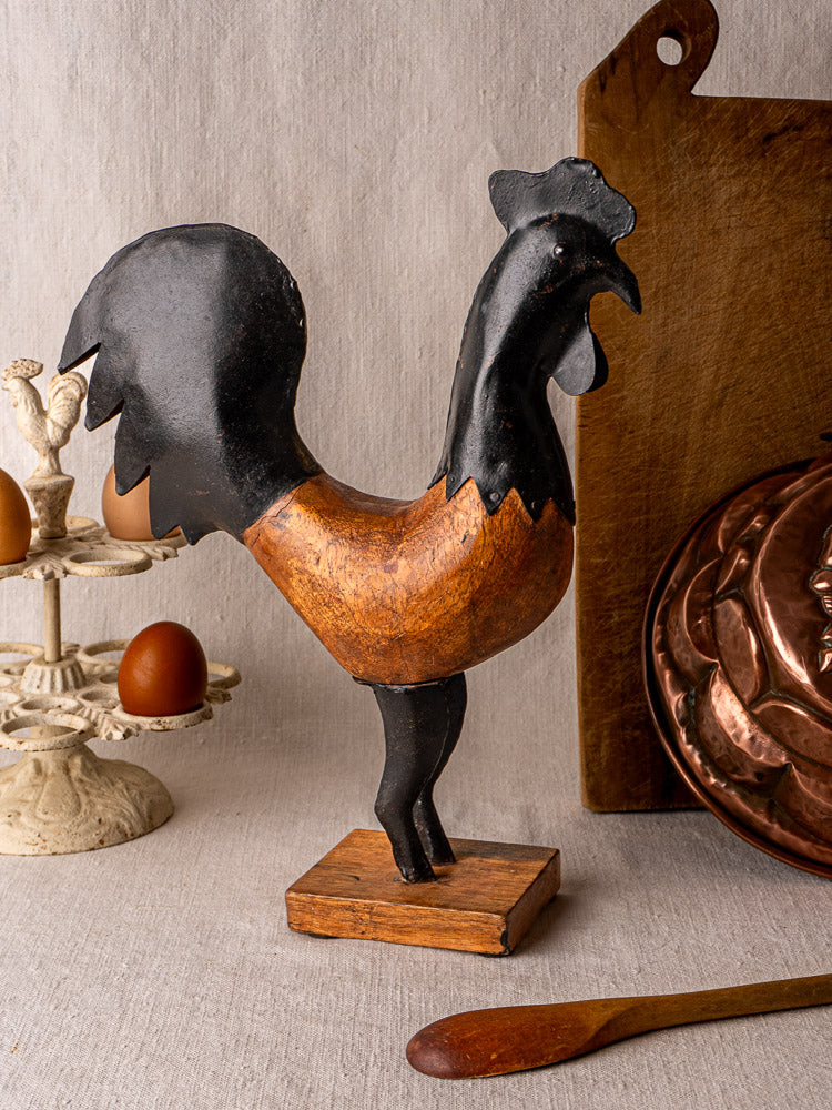 Antique French carved wood and metal rooster with black and brown paint on a table near eggs.