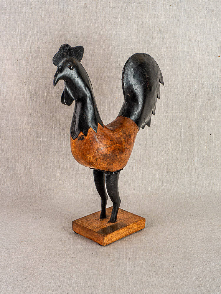 Antique French folk art rooster sculpture, carved wood with black and brown accents, on wooden base.