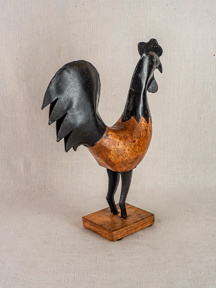 Antique French folk art carved wood and metal rooster on wooden base, beige background.