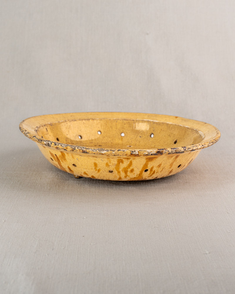 Antique French fruit strainer, 19th century, yellow-glazed earthenware with drainage holes and rustic finish on gray surface.