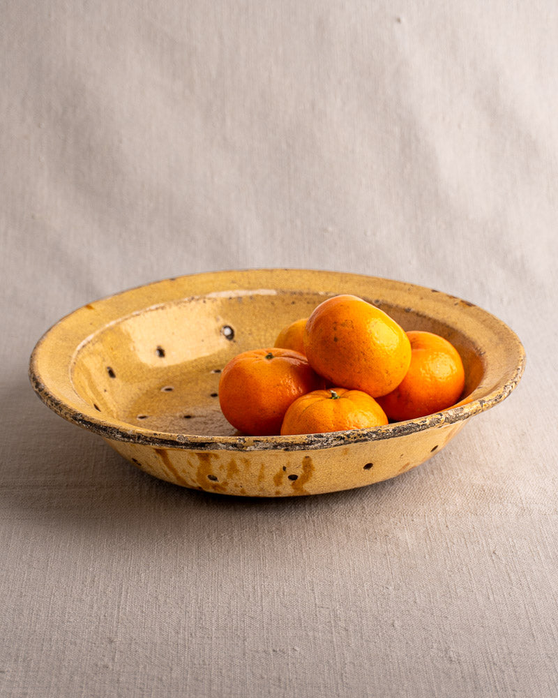 19th-century French glazed earthenware fruit strainer with five tangerines on neutral fabric, soft background.
