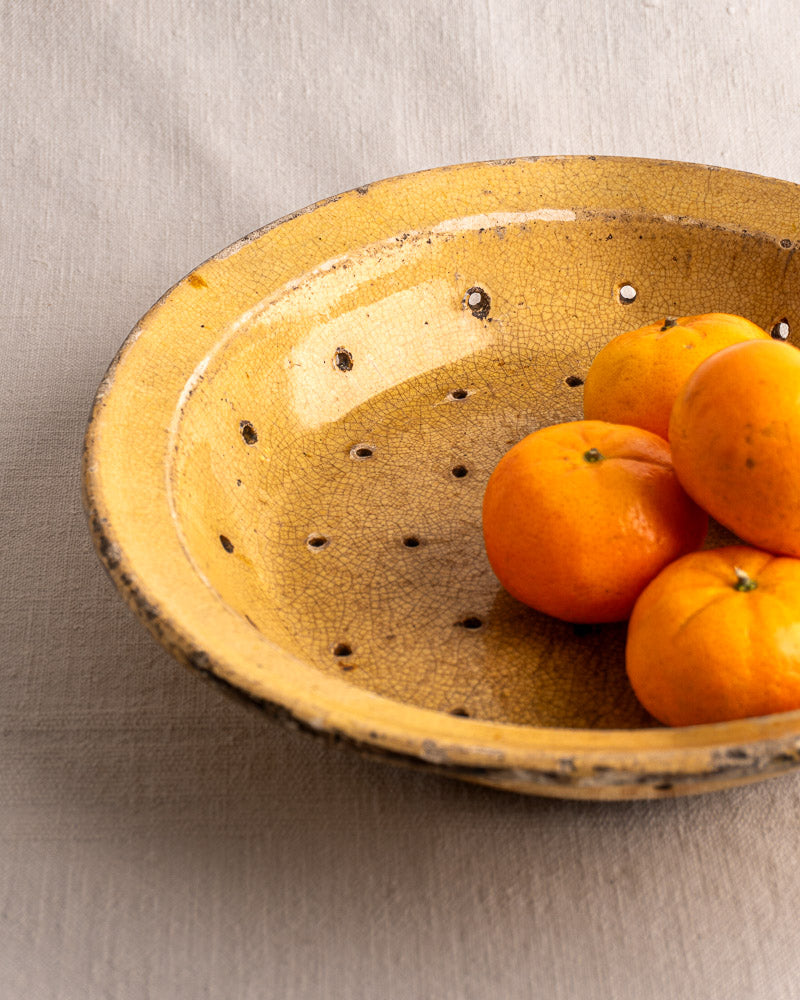 Antique French glazed earthenware égouttoir, round yellow plate with patterned holes, upright on a black stand.
