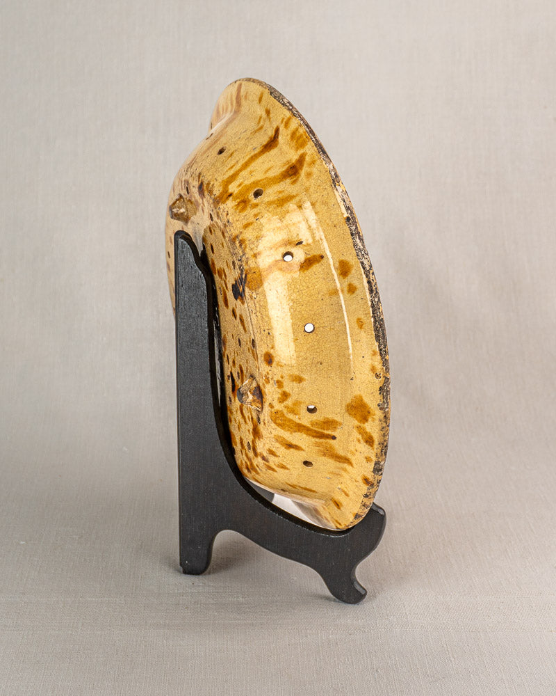 19th-century French glazed earthenware fruit strainer with tan and brown speckles, displayed on a black stand.